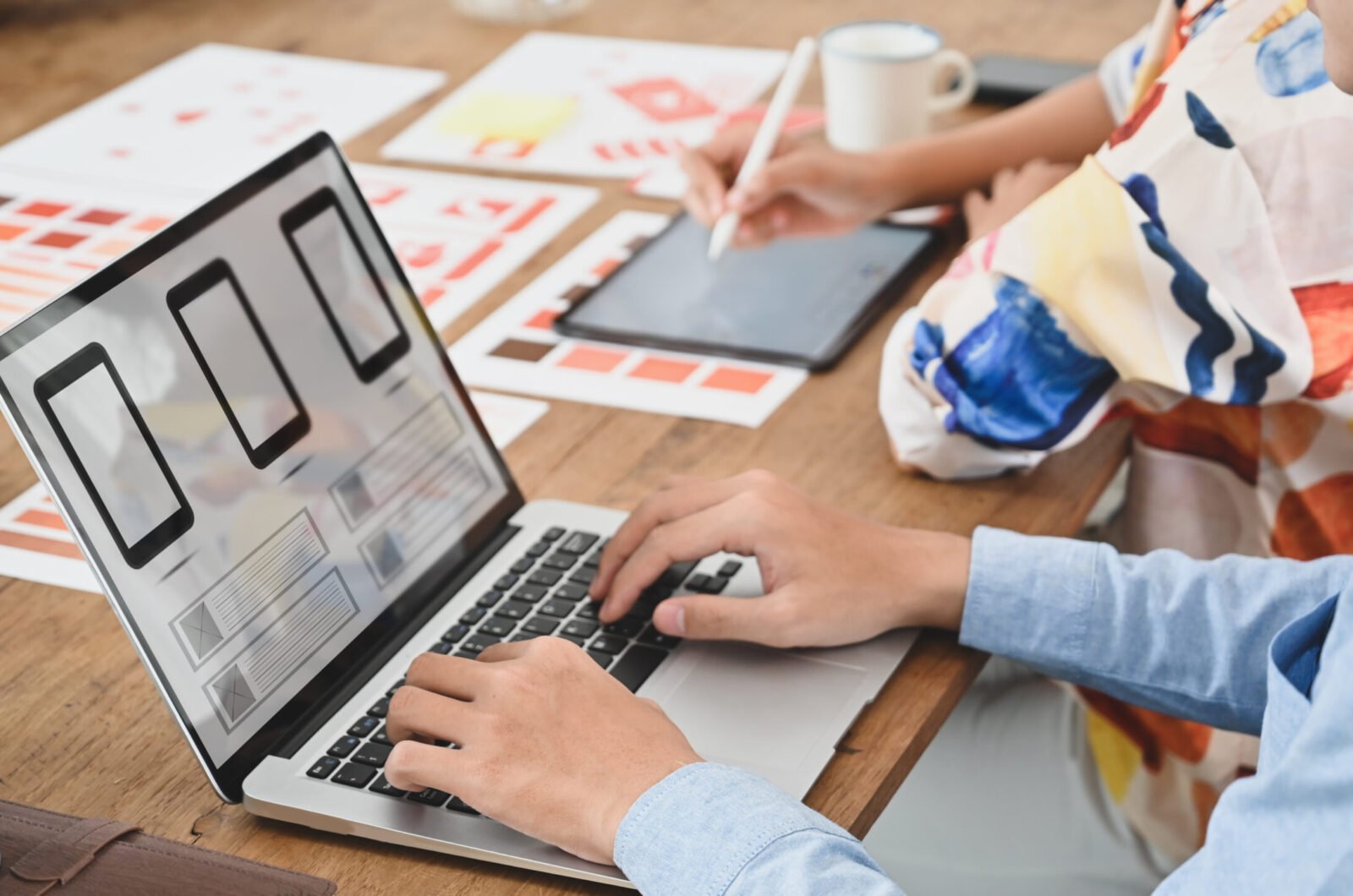 Cropped image of two people is using a computer laptop with an interface icon on the screen at the wooden table.