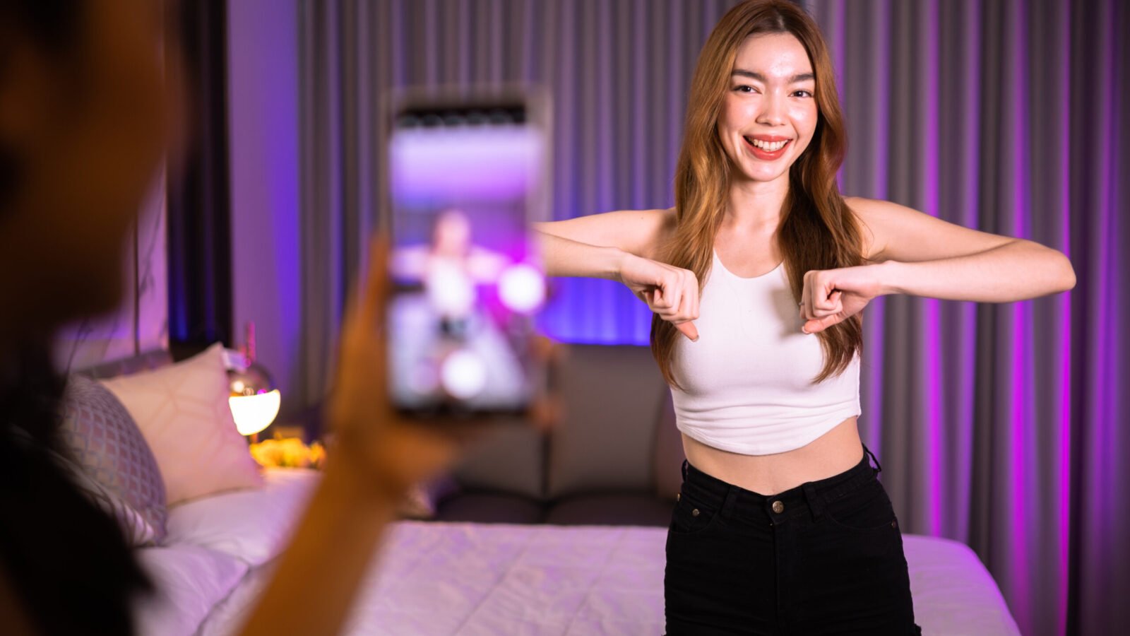 Asian and mixed race  female influencer shooting dance video for social media on mobile phone, having fun at home. To share video to social media application..